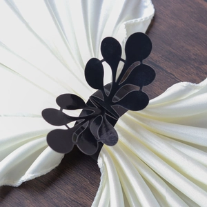 Detail view of the black laser-cut floral napkin ring on white satin fabric