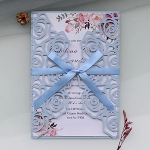 Close-up of laser-cut rose hollow invitation with blue satin bow and floral inner card