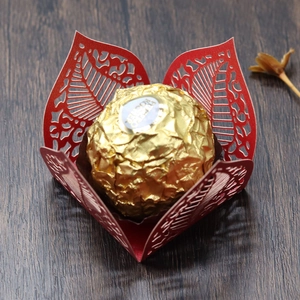 Macro detail of red laser-cut hollow leaf paper chocolate wrapper on dark wood background