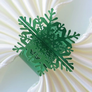 Close-up of green laser-cut snowflake napkin ring on a white folded cloth napkin