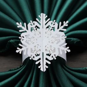 Close-up of laser-cut white pearlescent paper snowflake napkin ring on green satin