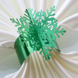 Macro detail of glossy green snowflake napkin ring on white silk fabric