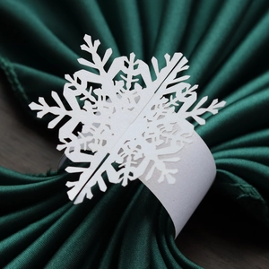 Close-up of white pearlescent snowflake paper napkin ring on dark green napkin