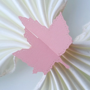 Close-up of laser-cut pink maple leaf paper napkin ring on white satin fabric