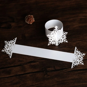 Laser-cut white paper snowflake napkin rings on a dark wood background with pine cone decor