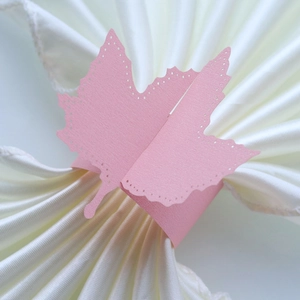 Close-up of laser-cut pink maple leaf paper napkin ring on a white silk napkin
