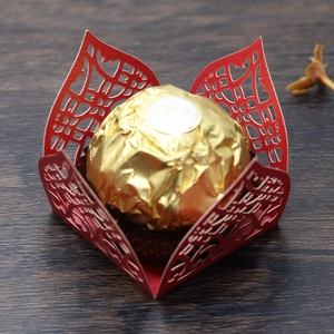 Macro detail of red laser-cut lace candy box with gold foil chocolate on wood background