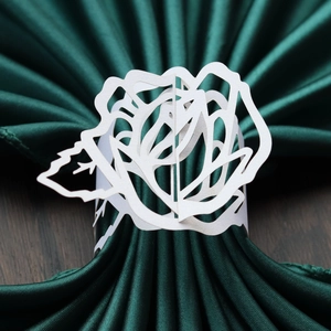 Detailed view of white laser-cut rose napkin ring on a dark green satin cloth