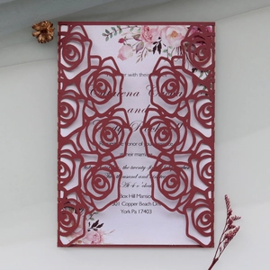 Macro detail of laser-cut rose hollow pattern on dark red wedding invitation card