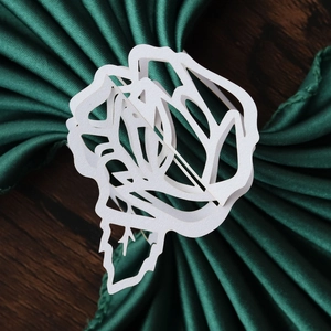 Close-up of white laser-cut rose paper napkin ring on dark green fabric and wood background