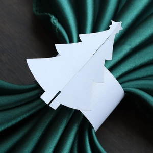 Détail du rond de serviette sapin blanc sur tissu vert et fond de table en bois sombre
