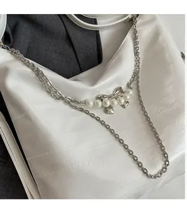 Detail der weißen Krokodilledertasche mit Silberkette und Perlen-Schleifen-Anhänger