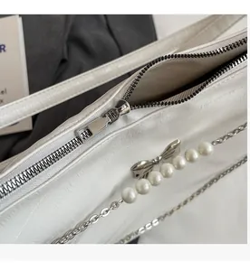 Detail eines silbernen Reißverschlusses mit Perlenkette und Schleifenanhänger an weißer Tasche