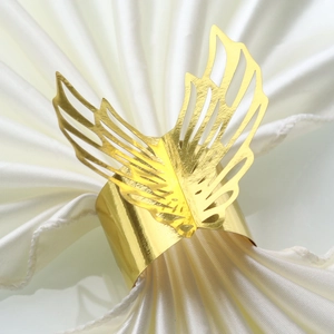 Macro view of gold laser-cut angel wing napkin ring on white satin fabric