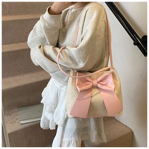 Détail d'un sac à bandoulière en paille tissée avec un grand nœud rose et bandoulière