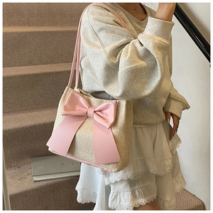 Détail du sac seau en paille beige avec un grand nœud en satin rose et doubles bandoulières