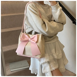 Détail d'un sac seau en paille avec un grand nœud rose, montrant la texture et la bandoulière