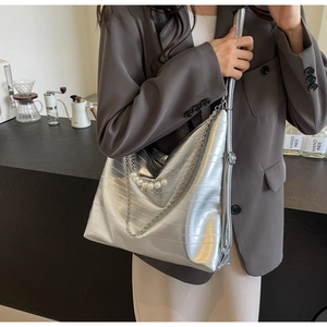 Detail der silbernen Metallic-Tasche mit horizontaler Struktur und Perlenanhänger