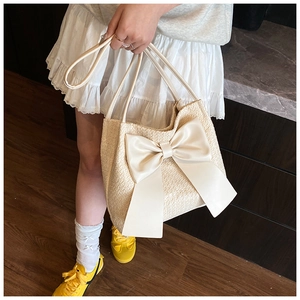 Détail du sac seau en paille d'été avec un grand nœud en satin crème et une texture tissée