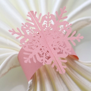 Macro detail of laser-cut pink snowflake paper napkin ring on white satin fabric