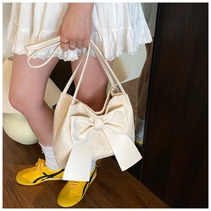 Gros plan d'un sac seau tressé beige crème orné d'un grand nœud décoratif en cuir
