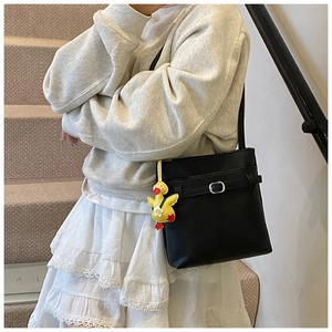 Détail du sac seau noir en cuir grainé avec un petit pendentif canard jaune sur la bandoulière