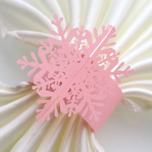 Detailed laser-cut pink snowflake napkin ring made of pearlescent paper on white cloth