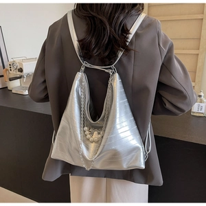 Detail eines silbernen Metallic-Rucksacks mit Textur, Metallketten und Perlen-Schleifen-Anhänger