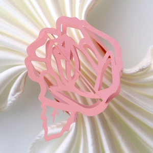 Macro detail of laser-cut pink paper rose napkin ring on a white fabric napkin