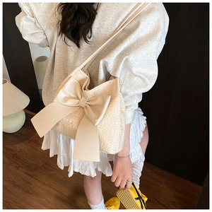 Détail du sac seau en paille crème avec un grand nœud en satin et une texture tissée élégante