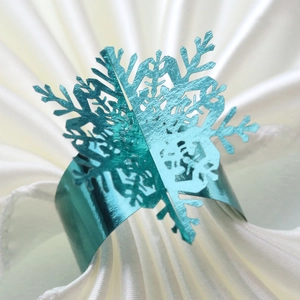 Close-up of a festive metallic teal snowflake napkin ring on a white folded cloth