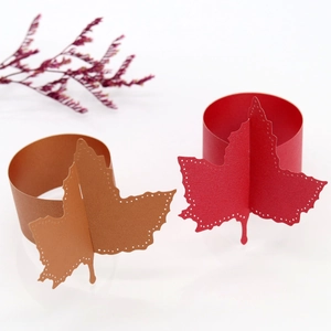 Close-up of laser-cut maple leaf paper napkin rings in gold and red festive colors