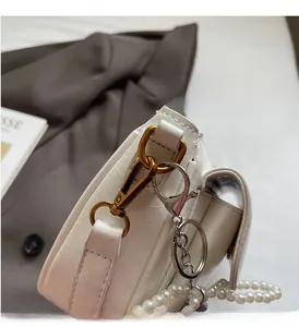 Detailed close-up of white leather handbag with vintage gold buckle and pearl strap