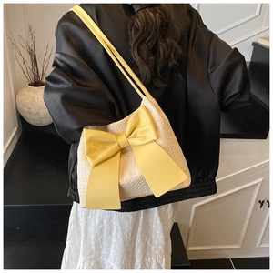 Détail d'un sac seau en paille avec un grand nœud en cuir jaune et fine bandoulière