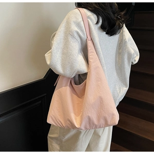 Detailed back view of a model wearing a light pink nylon hobo tote bag on the shoulder