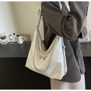 Detailansicht der weißen Tasche mit Krokoprägung, Perlen-Schleife und silberner Kette