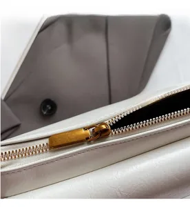 Detailed close-up of smooth vintage gold zipper on white textured leather pillow bag