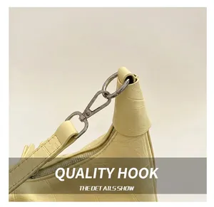 Detail of silver metal hook and textured leather texture on a light yellow shoulder bag