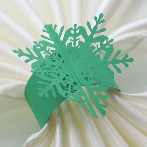 Detailed view of laser-cut green snowflake paper napkin ring on a white cloth napkin