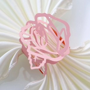 Macro detail of laser-cut pink paper napkin ring with floral hollow pattern on silk