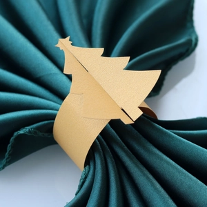 Détail d'un rond de serviette sapin de Noël doré sur un tissu en satin vert foncé