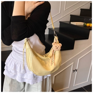 Close-up of pale yellow crocodile texture hobo bag with cute teddy bear charm detail