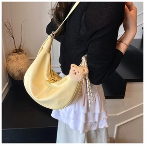 Detail of yellow crocodile embossed half-moon bag with cute teddy bear and ribbon charm
