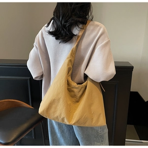 Mustard yellow nylon tote bag with wide strap shown on model's back in a minimalist room