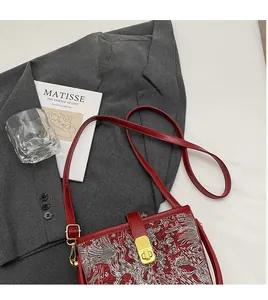 Detail shot of vintage red bucket bag featuring white embroidery and golden turn-lock closure