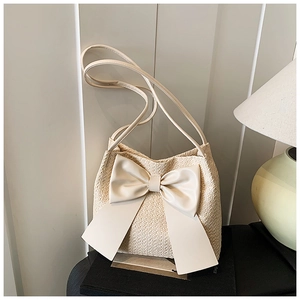 Vue détaillée du sac seau en paille crème avec un grand nœud décoratif en cuir synthétique