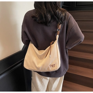 Detail einer großen Canvas Hobo-Tasche mit braunem Lederriemen und TCT-Logo an einem Modell