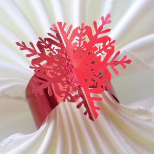 Close-up of a red metallic snowflake napkin ring on white fabric for Christmas decor