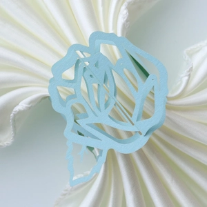 Detail of light blue laser-cut rose paper napkin ring on a white satin cloth
