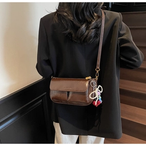 Detail of dark brown vintage crossbody bag with pearl bow and red heart charms on a model
